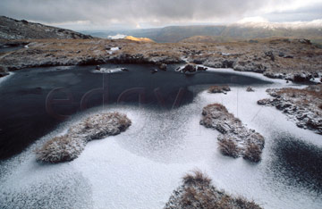 Comp image : ld02310 : Grass tufts on peat in a small frozen tarn covered with a sprinkling of snow, near the summit cairn of Place Fell