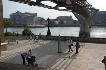 Comp image : lond010123 : Three small groups of people in the shadows under the Millennium Bridge over the River Thames in London, England, with a view across the river in the background