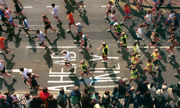 Comp image : mar000121 : London Marathon 2000: overhead view of the pack of runners passing over 'Ahead Only' painted on the road in the Docklands area of London, at about half distance