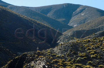 Comp image : mgun0823 : Looking up towards a peak in the High Atlas mountains of Morocco, with grass tufts in the foreground and a tiny lone figure standing in the mid distance