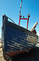 Bow view of an old blue fishing boat with worn paint in heavy shadow against a clear blue sky
