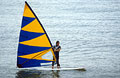 Windsurfer with blue and yellow sail on calm water