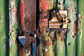 Close up of rusty metal on a peeling green painted corrugated iron gate