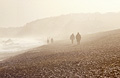 People in silhouette walking on the shingle at Dunwich, Suffolk, on the east coast of England