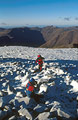 Looking east from snow-covered Scafell Pike in the English Lake District, with two figures in red in low winter sunshine