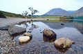Prominent rocks at the shore of Crummock Water, in the English Lake District, with a reflection of the distant fells in the background