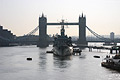 HMS Belfast moored on the River Thames in London, with Tower Bridge in partial silhouette in the middle distance