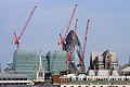 London city skyline, with gaunt red construction cranes in the sunshine in front of Sir Norman Foster's 'gherkin', against a blue sky