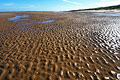 Wet rippled sand in sunshine on a deserted beach at low tide on the flat North Norfolk coast of England, under a clear blue sky