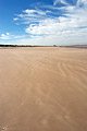 Flat deserted beach at low tide under a blue sky with scattered cloud, on the North Norfolk coast of England