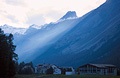 A shaft of evening sunlight across the misty blue mountains over a Swiss village