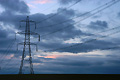Electricity pylon and cables silhouetted against stormy clouds, with a faint pink sunset glow