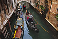 Gondolas passing in a narrow canal in Venice, Italy, with a bridge in the background; one moored, two others with gondoliers line astern