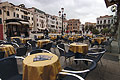 Chairs and round tables with yellow tablecloths outside a cafe in Campo San Stefano in Venice, Italy; a traditional 3-light Venetian street light behind